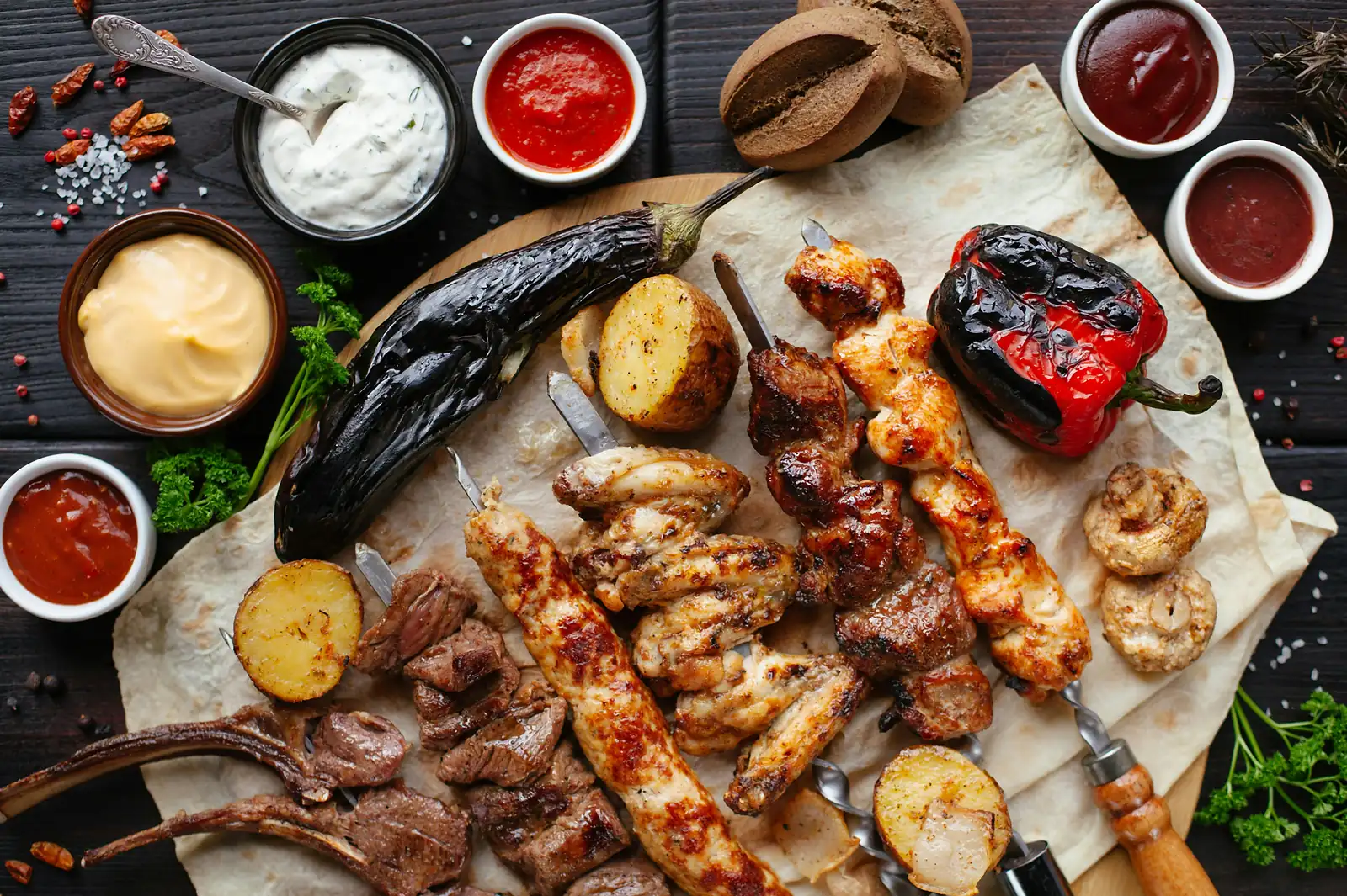 Grillplatte mit Spießen, Lammkoteletts, Aubergine und Paprika auf Fladenbrot, dazu mehrere Dips