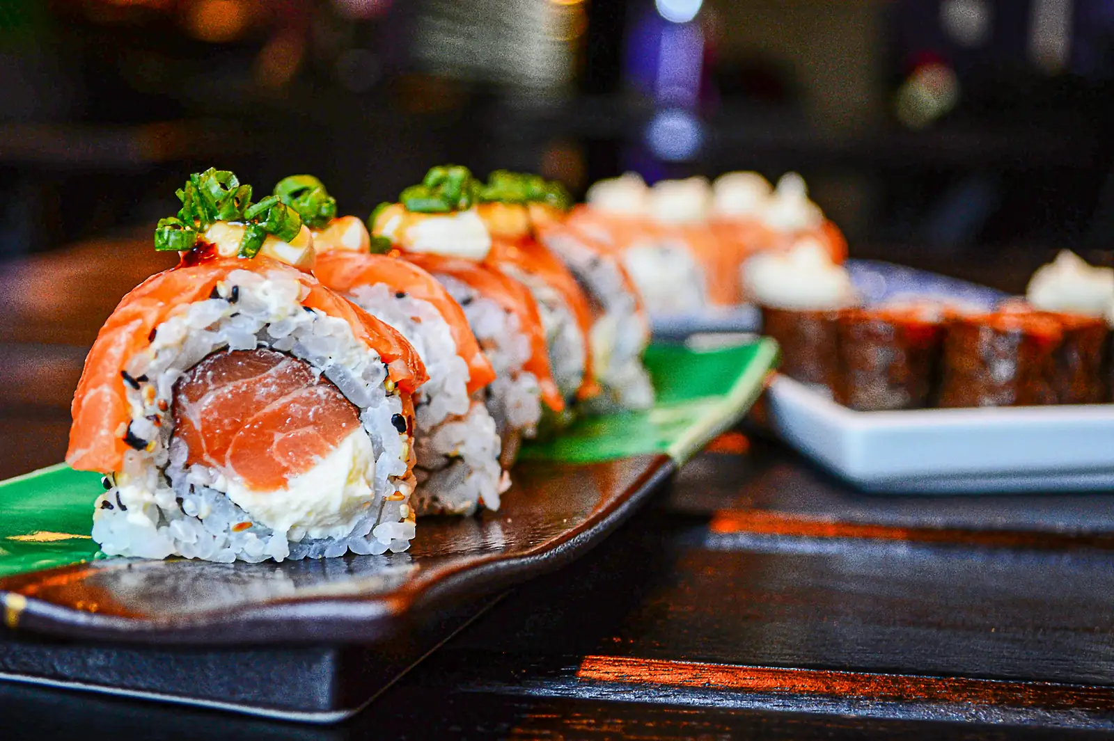 Nahaufnahme einer mit Lachs belegten Sushirolle auf dunklem Holz