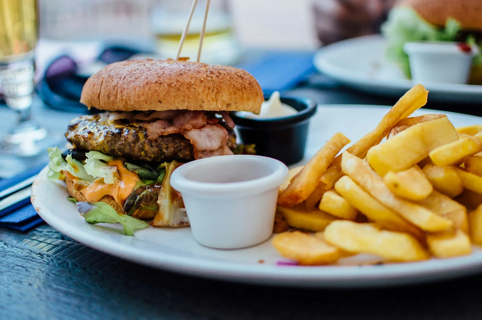 Burger mit Bacon und Salat auf einem Teller, daneben Pommes und zwei Dips
