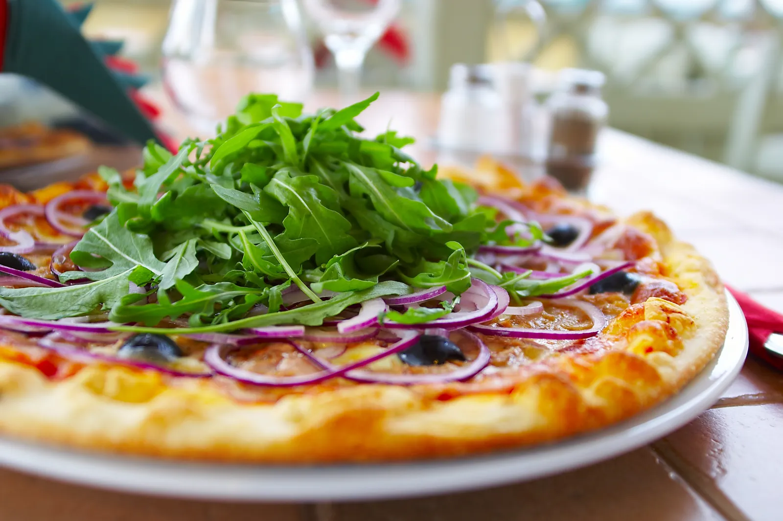 Pizza mit Rucola und roten Zwiebeln auf einem gedeckten Tisch