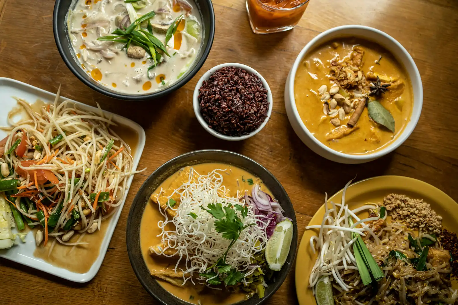 Thailändische Gerichte von oben: Currys, Pad Thai und Papayasalat auf einem Holztisch