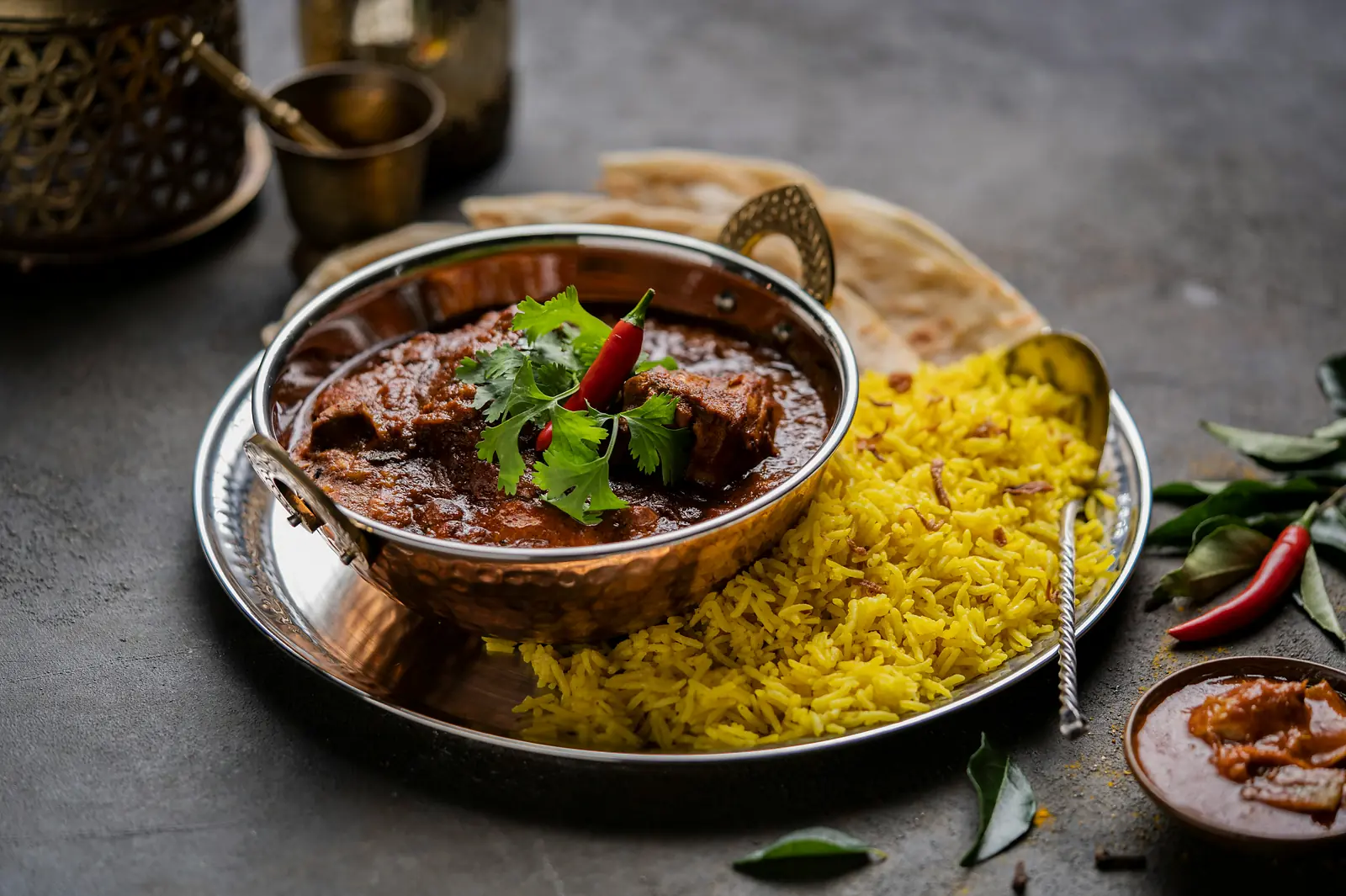 Curry in einer Kupferpfanne mit safrangelbem Reis, Naan und Curryblättern